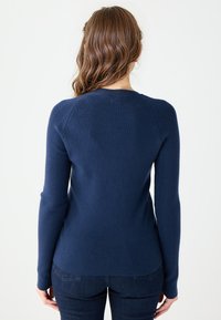 Granatowy sweter z dzianiny z długimi rękawami, okrągłym dekoltem i subtelną teksturą wzdłuż szwów. Wykończony dopasowanym krojem.