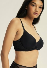 Czarny, wypełniony biustonosz z regulowanymi ramiączkami, koronkowym wykończeniem na dole i gładką tkaniną. Posiada usztywniony design z fiszbinami.