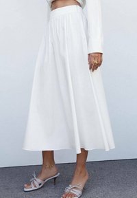 Jupe blanche de longueur midi avec un design plissé et une taille haute. Portée avec des talons ouverts gris clair avec un détail de bride.