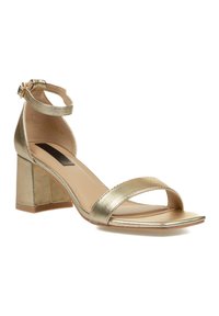 Sandalía de tacón metálico dorado con punta cuadrada, dos correas para el pie y un tacón bloque. Textura suave y correstrap de tobillo con detalle de hebilla.