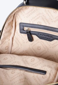 Interno di una borsa a mano in pelle nera con fodera in tessuto beige, caratterizzato da un motivo a logo ripetuto e una tasca con zipper dotata di un tirante in pelle nera.