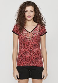 Chemise rouge à manches courtes avec motif floral noir et bordure noire, présentant un design brodé complexe autour de l'encolure.