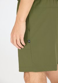 Vihreät lyhyet housut, jotka on valmistettu kevyestä kankaasta ja joissa on sivutasku. Housuissa on musta yksityiskohta ja yksinkertainen ommel helman reunassa.