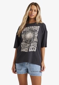 Sort oversized t-shirt med grafisk print af sol og tekst, kort ærmer, lavet af bomuld, parret med lyseblå denim shorts.