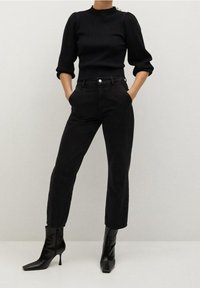 Haut noir en maille côtelée avec un col montant, associé à un jean noir taille haute et des bottines noires pointues. Design élégant et ajusté.