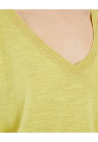 Kadar blizu gornjeg dijela prsnog koša osobe koja nosi svijetlozelenu pletenu majicu s V izrezom.