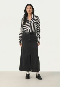 Sort denim maxi nederdel med frontslids, parret med en sort og hvid stribet skjorte med knapper, afsluttet med et sort bælte og loafers.