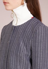 Abito a righe navy e bianco con texture, dotato di un alto colletto a coste bianche, chiusura con zip dorata e due bottoni circolari.