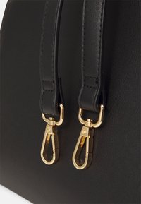 Lähikuva kahdesta mustasta nahkavarresta, joissa on kiiltävät kultaiset metalliset kääntöklipsit, kiinnitettyinä sileään mustaan nahkapintaan.