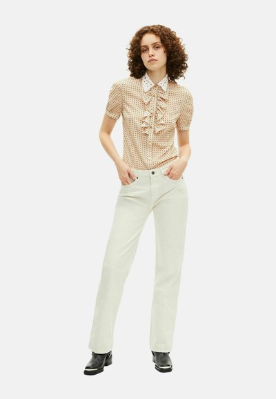 Perzikkleurige blouse met stippen, voorzien van voorrimpelingen en een witte kraag, gecombineerd met lichtgekleurde wijde broekspijpen en zwarte enkelboots.