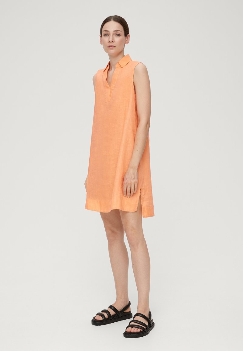 Ärmelloses Kleid aus weichem orangefarbenem Leinen mit einem Kragen, seitlichen Schlitzen und einer lockeren Passform, kombiniert mit schwarzen Riemchensandalen.