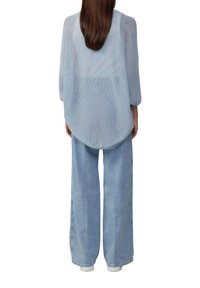 Lichtblauwe mesh oversized shirt met driekwartmouwen, gecombineerd met loszittende lichtblauwe spijkerbroek en witte sneakers.