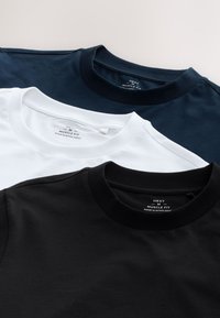 Trois t-shirts à col rond pliés en bleu marine, blanc et noir, étiquetés medium muscle fit, posés à plat sur un fond clair.