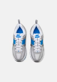 Baskets Nike Vomero 5 avec une tige en mesh gris, des accents bleus, des lacets blancs et une languette rembourrée, dotées d'une semelle intermédiaire gris clair et d'une semelle extérieure en caoutchouc.