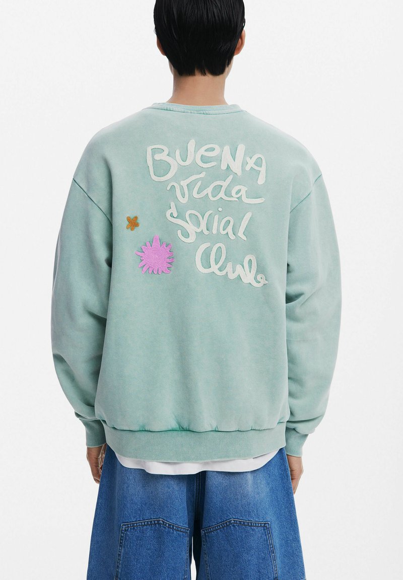 Sweatshirt vert menthe au fit surdimensionné, avec un texte brodé et des appliqués floraux colorés à l'arrière. Poignets et ourlet côtelés.