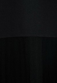 Indumento nero con una parte superiore texture e una parte inferiore trasparente e fluida. Il tessuto è liscio con un leggero motivo a coste nella parte superiore.