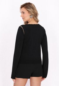 Top negro de manga larga con cuello en forma de escalope y acento decorativo, con textura de punto y diseño ajustado.