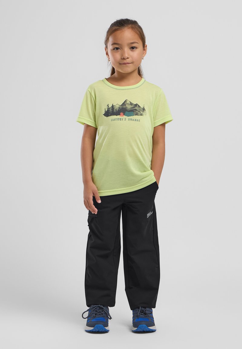 T-shirt vert clair avec un graphique de montagne et le texte "Nomades de la Nature", associé à un pantalon cargo noir et des chaussures bleues. Fond uni.