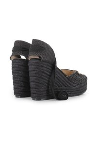 Zapatos de cuña tejidos en negro, con un upper texturizado, tacón envuelto en cuerda y un adorno de tela en forma de flor decorativa a un lado.