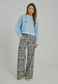 Cămașă scurtă, cu nasturi, de culoare albastru deschis, cu tiv alb, purtată cu pantaloni evazați, cu talie înaltă, având un model cu imprimeu de șarpe alb-negru.