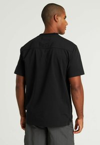 T-shirt nero a maniche corte con scollo rotondo, dotato di un pannello posteriore rinforzato e fessure laterali per maggiore comfort e traspirabilità.