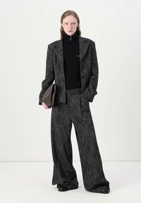 Siva blazer z vzorcem in širokimi hlačami, v kombinaciji s črnim zip-up turtleneckom in rjavim clutchom. Tkanina ima teksturiran zaključek.