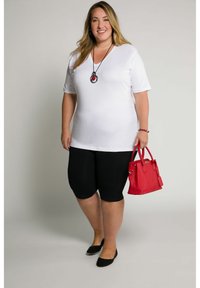T-shirt bianco a scollo a V, pantaloni corti neri e ballerine nere. Una borsa rossa e una collana con un pendente circolare. Design minimalista e texture liscia.