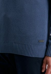 Dunkelblauer gestrickter Pullover mit einem strukturierten Muster, geripptem Saum und Bündchen, versehen mit einem kleinen metallischen Logopfad in der unteren linken Ecke.