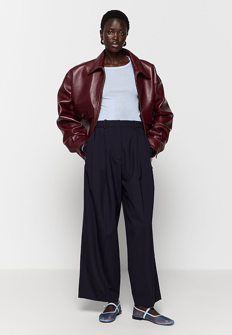 Bordowa skórzana krótka kurtka na jasnoniebieskiej koszulce, zestawiona z wysoko taliowanymi granatowymi szerokimi spodniami i niebieskimi płaskimi butami na kostkę.