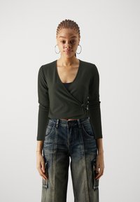 Haut enroulé à manches longues de couleur vert foncé à côtes, associé à un jean cargo large de couleur bleu délavé avec poches latérales et coupe décontractée.