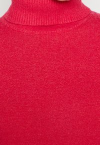 Roter Strickpullover mit Rollkragen, der über einen gerippten Kragen und eine weiche Textur verfügt, mit einer gleichmäßigen, glatten Verarbeitung des gesamten Stoffes.