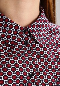 Röd och marinblå mönstrad skjorta med små blommönster, med en knäppbar krage, svarta knappar och en slät tygtextur.