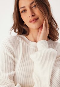 Maglione a coste crema con maniche lunghe e ampia svasatura e scollatura rotonda, caratterizzato da una consistenza morbida e una leggera lucentezza.