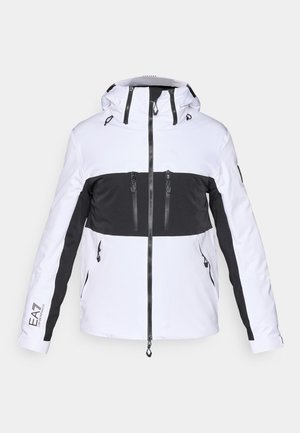 Casaco de ski branco e preto com capuz, apresentando bolsos com fecho éclair, design de blocos de cor contrastantes e detalhes texturizados nos ombros.