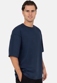 Marineblauw T-shirt met korte mouwen van gladde stof. Rond halsontwerp met een ontspannen pasvorm. Handen in zakken, effen zonder patronen of accenten.