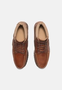 Paire de chaussures décontractées en cuir marron à lacets, avec col rembourré et coutures visibles, vues de dessus sur un fond blanc.