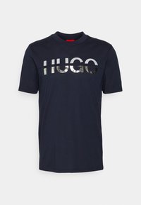 Navy blue cotton T-shirt with short sleeves and a round neck. Features a reflective silver "HUGO" logo across the chest.