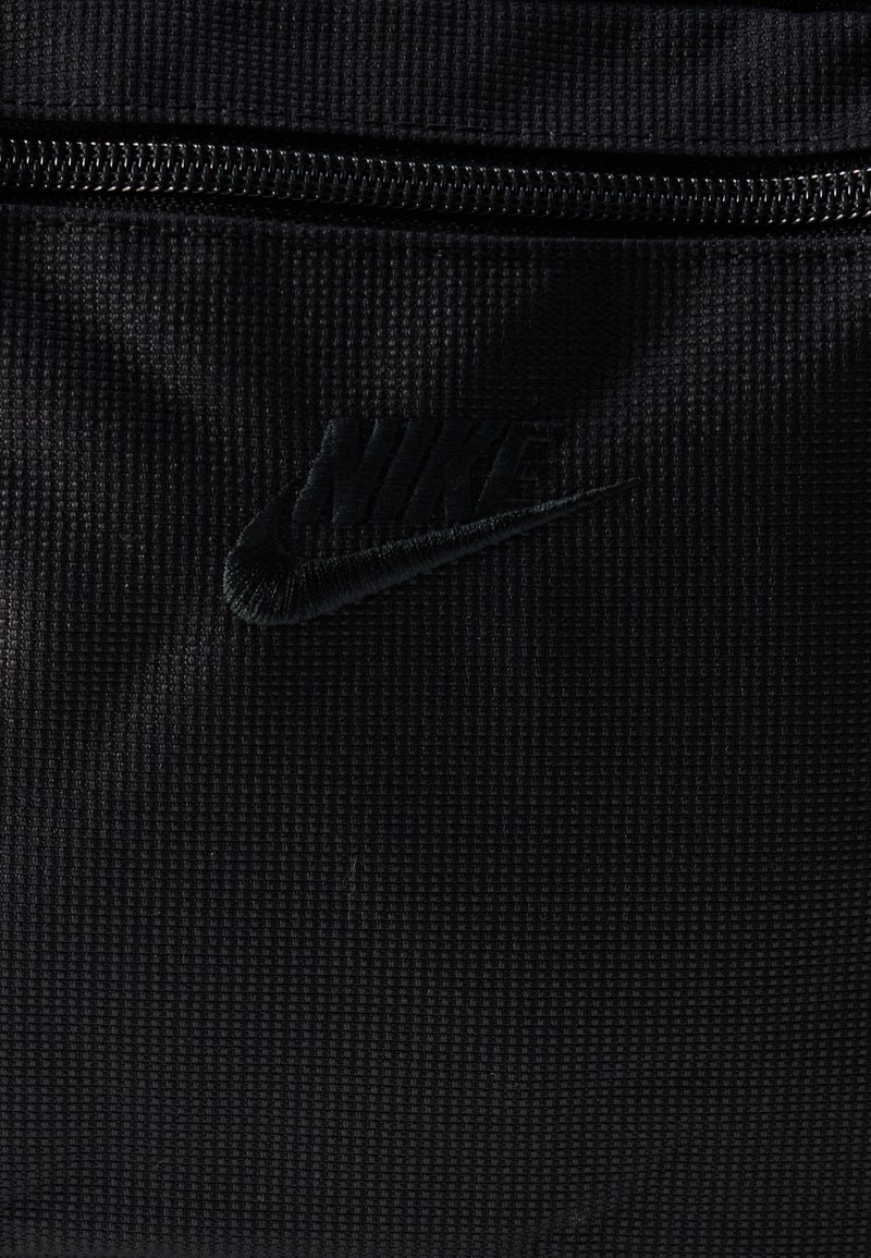 Tissu noir texturé avec un logo Nike brodé discret et une fermeture éclair noire au-dessus.