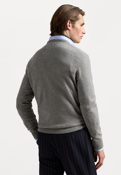Pull en maille grise avec un col rond, des poignets et un ourlet côtelés. Porté par-dessus une chemise à col bleu clair, associé à un pantalon à rayures.