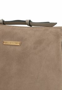 Borsa in suede marrone con una superficie liscia, dettagli in pelle e una placca dorata con la scritta "PICARD" attaccata sul davanti.