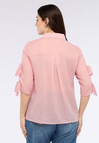 Jasnoróżowa koszula z rękawami ¾, z wiązanymi akcentami na rękawach, kołnierzu oraz plisą z tyłu. Miękki, delikatny materiał.