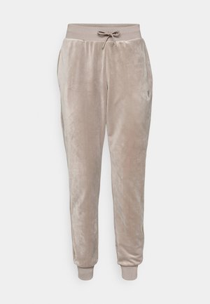 Velvet joggers in light beige, featuring an elastic waistband with drawstring, side pockets, and ribbed cuffs. Subtle branding on the left side.