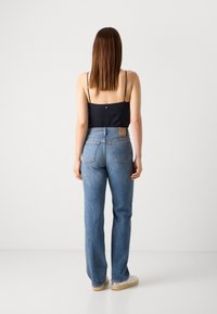Donkerblauw mouwloos topje met dunne bandjes, gecombineerd met lichtblauwe recht gesneden jeans, zichtbare stikdetails en een tan leren accent op de achterkant.