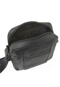 Bolso cruzado de cuero negro con acabado texturizado, cierre de cremallera y un compartimento interior. Presenta un logo troquelado en la parte frontal.