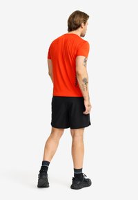 Röd kortärmad tröja med rund halsringning, ihop med svarta shorts. Tröjan har en logotyp med mörk text på ryggen.