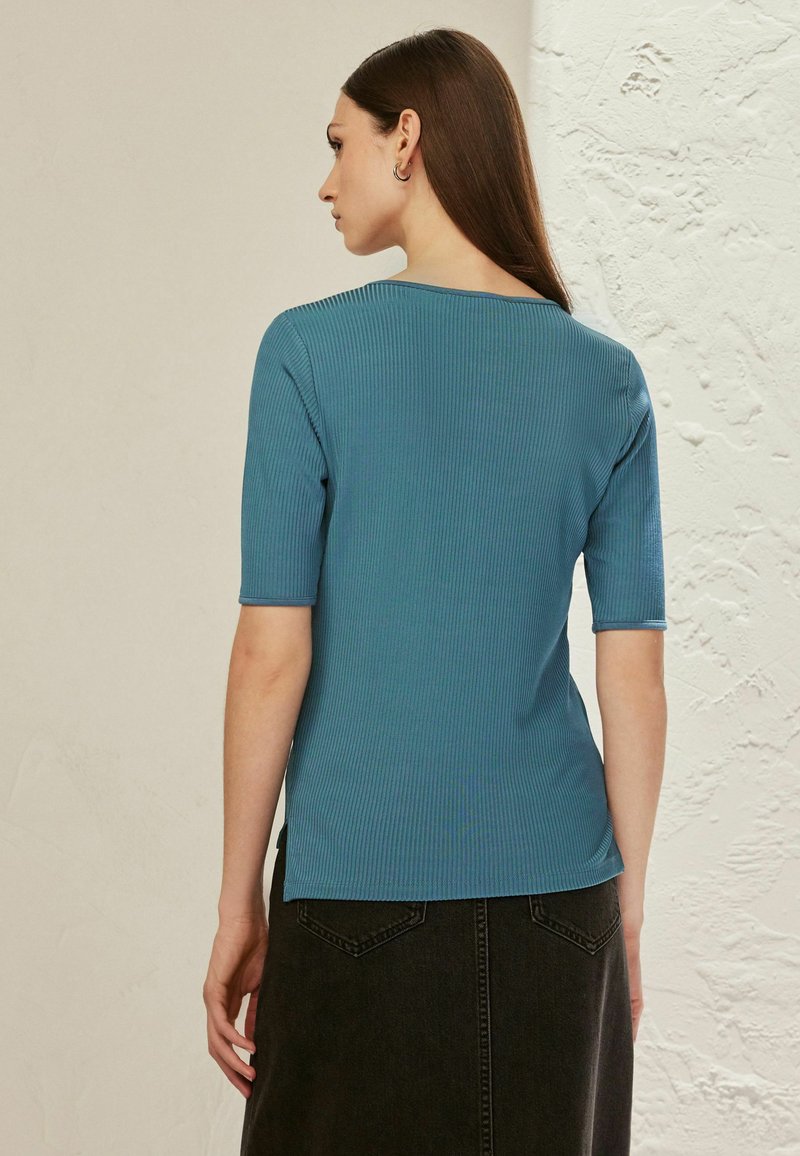 Geribbelde teal top met een ronde halslijn en korte mouwen, gestyled met een aangesloten silhouet, gecombineerd met een donkere rok en subtiele naaddetails.