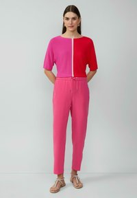 Fuchsia en roze kleurblokken trui met korte mouwen, gecombineerd met roze jogpants met trekkoord. Model draagt platte sandalen en staat tegen een neutrale achtergrond.