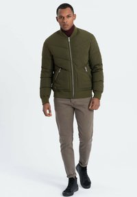 Olivgrön puffjacka med quiltat mönster, dragkedjestängning, två framfickor. Parat med beige byxor och svarta sneakers.
