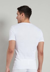 T-shirt bianco in cotone con maniche corte, design aderente, scollo rotondo. Texture liscia senza motivi o decorazioni visibili.
