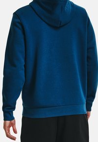 Haut à capuchon en polaire bleu avec un cordon de serrage, des poignets et une taille côtelés, présentant une texture lisse et un design uni.